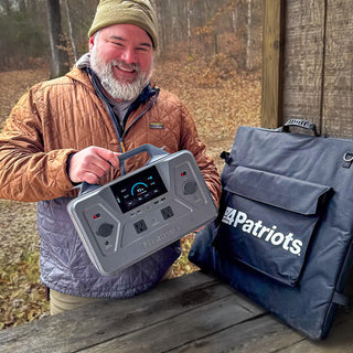 Survival influencer Craig Caudill holding the Patriot Power Solar Generator 1200 with its folding solar panel bag outdoors in fall woods; links to 4Patriots off-grid power blog content