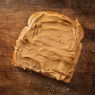 Peanut Butter Powder #10 Can mixed and spread thickly on a slice of toast on a wood board, an easy protein-rich survival food for everyday meals