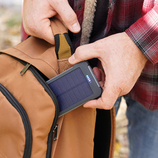 Man slips the Patriot Power Cell-CX Portable Solar Power Bank into a backpack pocket, compact portable solar charger for off-grid hiking and emergency backup power