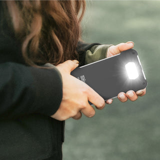 Woman holds the Patriot Power Cell-CX Portable Solar Power Bank using its bright built-in LED flashlight outdoors, off-grid emergency solar charger and survival light