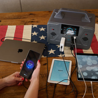 Patriot Power Generator 1200 portable power station charging a phone, two tablets and a laptop at once on an American flag table runner