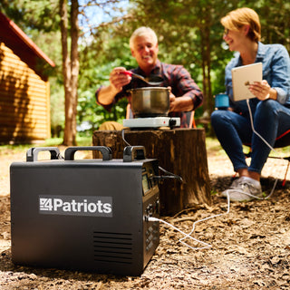 Patriot Power Solar Generator 1800 at a wooded campsite running a hot plate while a couple cooks and charges a tablet, off-grid portable solar backup power