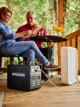 Patriot Power Solar Generator 1800 powering a cooling fan on a cabin porch as a couple relaxes, portable solar generator for off-grid and emergency backup power