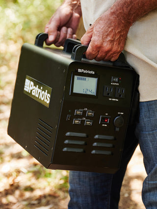 Man carrying the Patriot Power Solar Generator 1800 portable solar power station by its handle through the woods for off-grid and emergency backup power