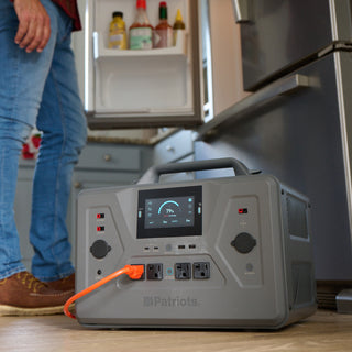 Patriot Power Generator 2200X on a kitchen floor with an orange cord powering a fridge, man standing behind, solar generator for home backup