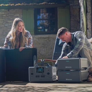 Expansion Battery Pack for Patriot Power Generator 2200X, couple on a stone cottage porch setting up two stacked packs, the 2200X and a 200W solar panel for backup power