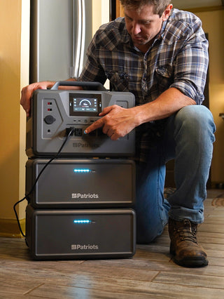 Expansion Battery Pack for Patriot Power Generator 2200X, two stacked packs under the 2200X as a kneeling man powers his fridge for indoor blackout backup