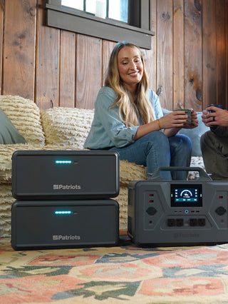 Expansion Battery Pack for Patriot Power Generator 2200X, two stacked packs beside the 2200X as a couple relax in their living room with off-grid emergency backup power