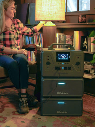 Expansion Battery Pack for Patriot Power Generator 2200X, two packs stacked under the 2200X powering a lamp a woman switches on during an indoor blackout backup