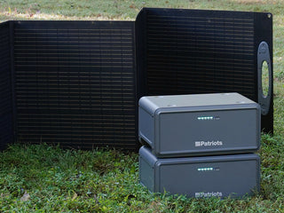 Expansion Battery Pack for Patriot Power Generator 2200X, two stacked packs on grass in front of an unfolded 200W solar panel for portable off-grid emergency power