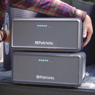 Expansion Battery Pack for Patriot Power Generator 2200X, close-up of a man lifting the top of two stacked packs from a truck bed for off-grid solar backup power