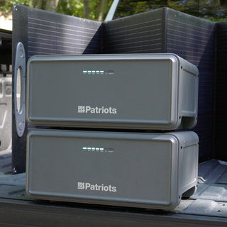 Expansion Battery Pack for Patriot Power Generator 2200X, two stacked packs loaded in a truck bed with a 200W folding solar panel behind for portable emergency power