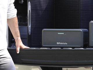 Expansion Battery Pack for Patriot Power Generator 2200X, a man loading a pack onto a truck tailgate beside a 200W folding solar panel for portable off-grid power