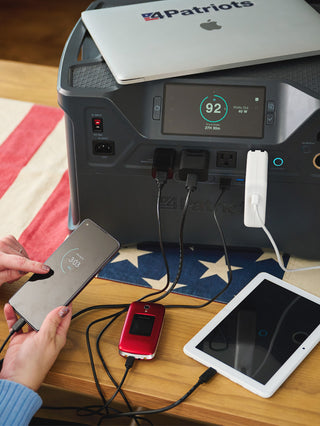 Patriot Power Solar Generator 2000X charging a laptop, smartphone, tablet and flip phone at once, showing this portable solar generator's off-grid emergency backup power