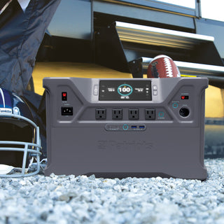 Patriot Power Solar Generator 2000X portable solar power station charged to 100% on gravel at an RV tailgate with football helmet and ball, off-grid emergency backup power