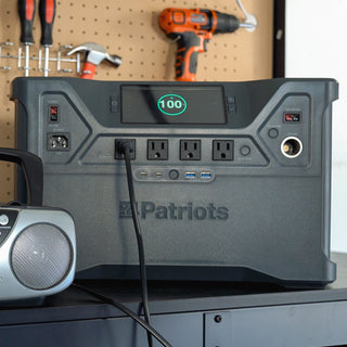 Close-up of the Patriot Power Solar Generator 2000X on a garage bench with pegboard tools and a radio plugged in, portable solar generator for off-grid backup power