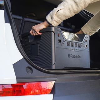 Person loading the Patriot Power Solar Generator 2000X into an SUV trunk by its handle, portable solar power station ready for off-grid travel and emergency backup power