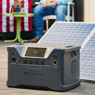 Patriot Power Solar Generator 2000X charged to 100% on a deck with folding solar panel, American flag and seated man, portable off-grid emergency backup power station