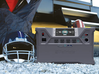 Patriot Power Solar Generator 2000X portable solar power station at a game-day RV tailgate beside a football helmet and jersey, off-grid emergency backup power