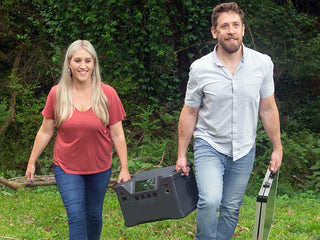 Patriot Power Solar Generator 2000X carried outdoors by a smiling couple with a folding solar panel, lightweight portable solar generator for off-grid emergency backup power
