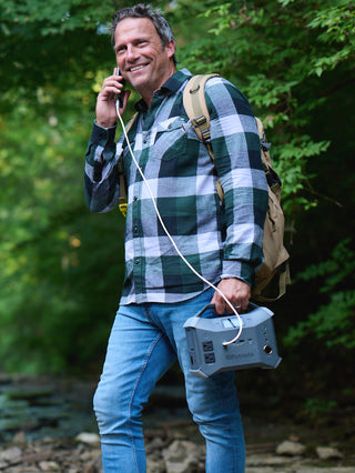 Patriot Power Generator 1800 + Sidekick Kit: hiker carries the Sidekick portable power station by a stream, phone charging on the go for off-grid backup power