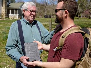Patriot Power Voyager XL Solar Power Bank handed from father to son on a farm, rugged portable solar charger for off-grid and emergency power backup
