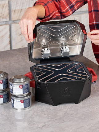 Woman opening the RescueHeat Emergency Space Heater & Stove on a kitchen counter beside 6HR fuel cans, an easy-to-use emergency heater and cook stove for power outages