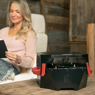 RescueHeat Emergency Space Heater & Stove warming a living room as a woman reads nearby, a quiet indoor emergency space heater for power outage preparedness