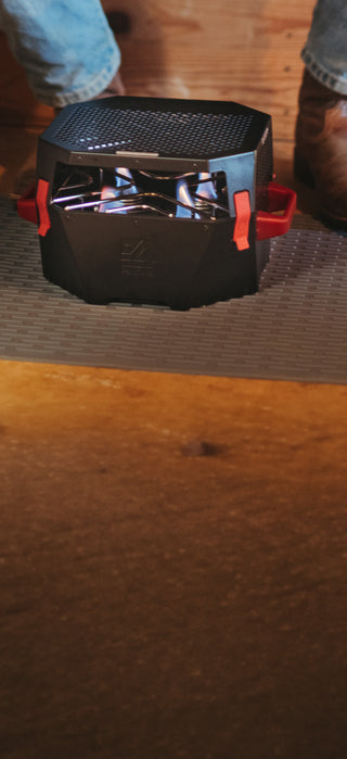 4Patriots portable emergency heater burning with blue flames on a floor mat as a person in boots stands nearby, an indoor-safe fuel heater for off-grid warmth and disaster preparedness