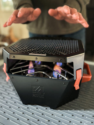 Hands warming over the RES heater fueled by RescueHeat Canned Heat & Chafing Fuel with blue flames, indoor emergency heating for power outages and off-grid warmth