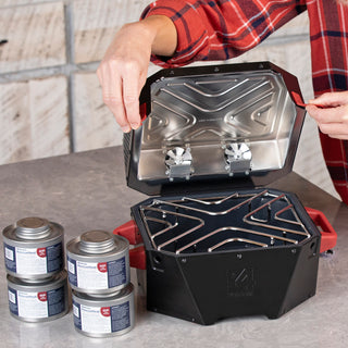 Opening the RES emergency stove in a kitchen beside four RescueHeat Canned Heat & Chafing Fuel cans, canned cooking fuel for power outage preparedness