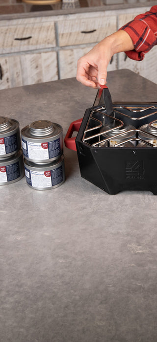4Patriots RescueHeat 6HR Fuel cans stacked on a kitchen counter beside the RescueHeat emergency heater loaded with cans under its grate, indoor-safe emergency heat and chafing fuel for preparedness