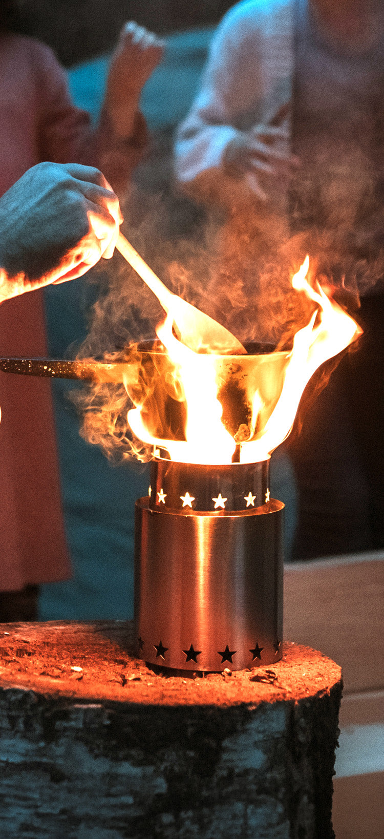 Translation missing: en.StarFire Portable Camp Stove, a stainless steel wood-burning stove with star cutouts blazing on a tree stump as a hand stirs a pot over the flames, off-grid emergency cooking for disaster preparedness