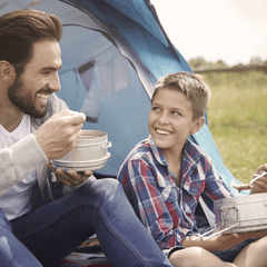 Man and boy eating 4Patriots prepared food outside in a camping tent.