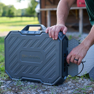 Silver Star Emergency Survival Package: man plugging a solar panel cable into the 4Patriots AlphaCase power station outdoors on gravel, portable solar generator