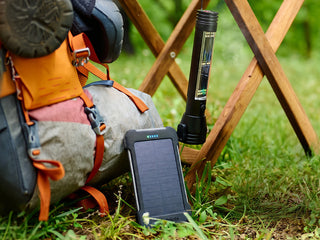 Silver Star Emergency Survival Package: 4Patriots solar power bank and a HaloXT flashlight hanging from a camp chair beside a backpack on grass, off-grid gear
