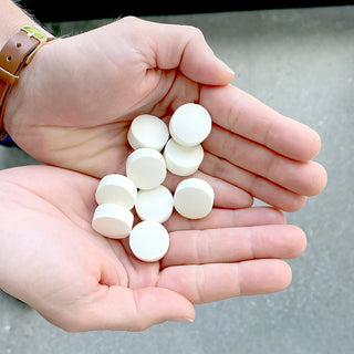 Two open palms holding eight white 4Patriots Sur-Vital Tabs lemon-flavored survival food supplement tablets