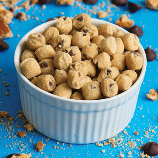 White ramekin filled with 4Patriots Freeze-Dried Chocolate Chip Cookie Dough Bites surrounded by chocolate chips and cookie crumbles on a blue surface