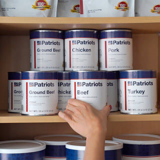 Hand taking a 4Patriots Beef can from a pantry shelf stocked with Ultimate Meat Medley cans, shelf-stable protein on hand