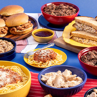Overhead table of Ultimate Meat Medley meals: pulled pork sliders, ground beef, shredded chicken, spaghetti and a melt on blue