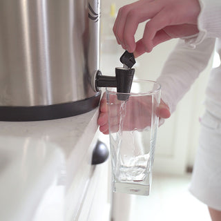 Patriot Pure Ultimate Water Filtration System Replacement Parts spigot in use as a hand fills a glass with purified water from the stainless dispenser