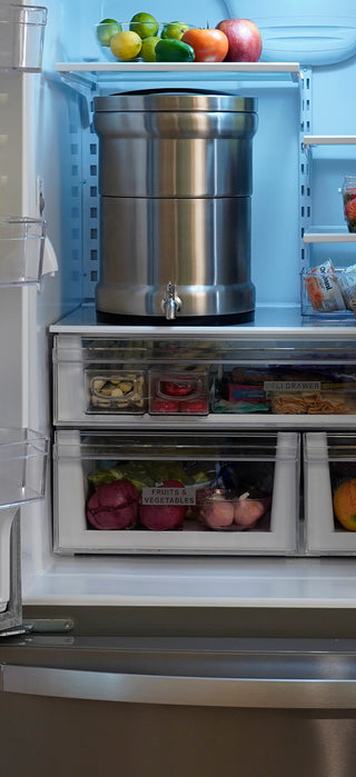 Vertical view of the Patriot Pure Ultimate Water Filtration System inside a refrigerator above the produce drawers, sized to fit on a standard fridge shelf
