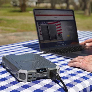 Patriot Power Voyager XL solar power bank charging a laptop on a picnic table, portable solar power and off-grid emergency backup power for disaster preparedness