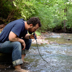 Man drinking water at a stream using the Patriot Pure Personal Water Filter
