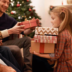 Child holding presents while someone hands her another present.
