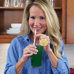 Woman drinking Patriot Power Greens with a straw in kitchen.