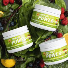 Three Patriot Power Greens canisters sitting over fruit and vegetables.