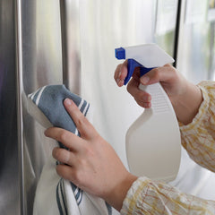 Someone spraying the handle of a fridge with sanitizing solution.