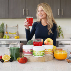 SunUp to SunDown Bundle on a countertop with each canister next to a glass of each supplement. Mindy in the background holding a glass of Patriot Power Reds.