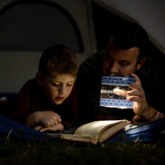 Man holding the SoLantern Air Inflatable Solar Lantern & Charger while a boy reads in the dark.